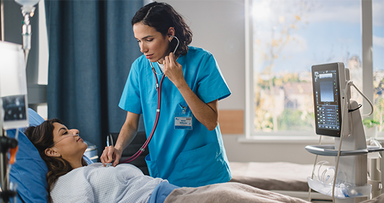 Female patient in hospital bed with female medical professional checking heart with a stethescope