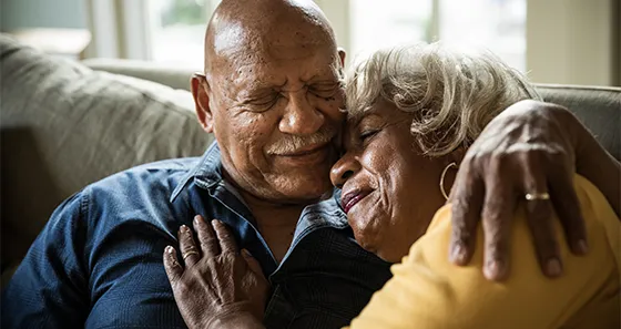 Older man and woman embracing on couch and smiling