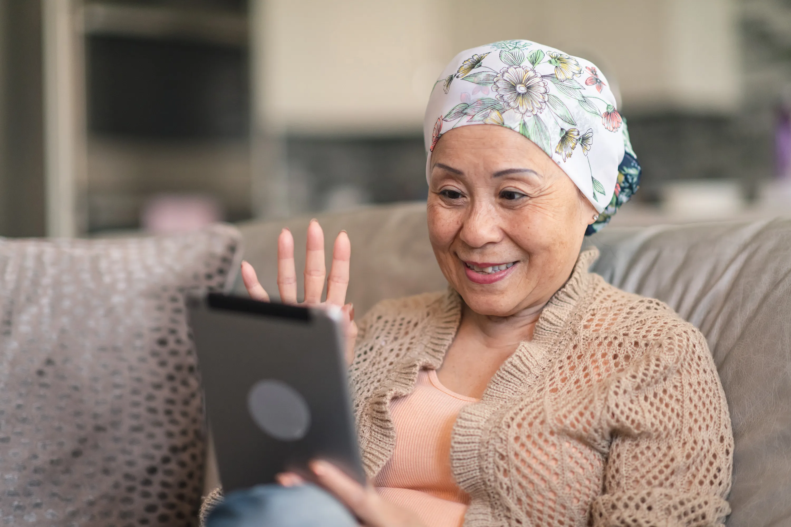 Older woman with headscarf sitting on couch using tablet computer and smiling